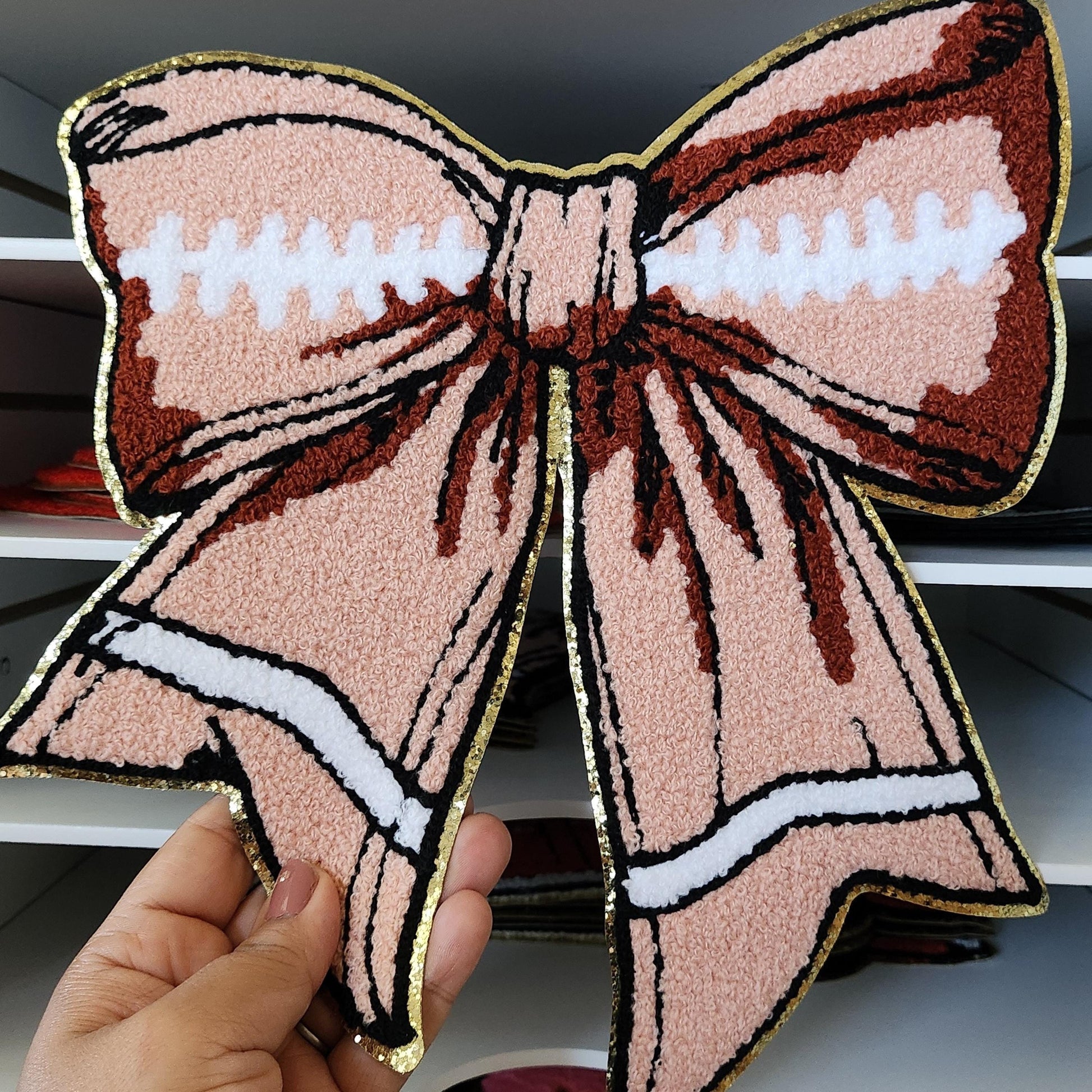 Sports Full Size Chenille|Sequin| Iron On|Embroidered| Chenille Patches| Chenille Patches| Chenille Patch Sweater| Chenille Patch Iron On

A large pink and brown bow with a white trim. The bow is made of a fluffy material and has a gold outline. The bow is a decorative item and can be used for crafts, clothing, or home decor.