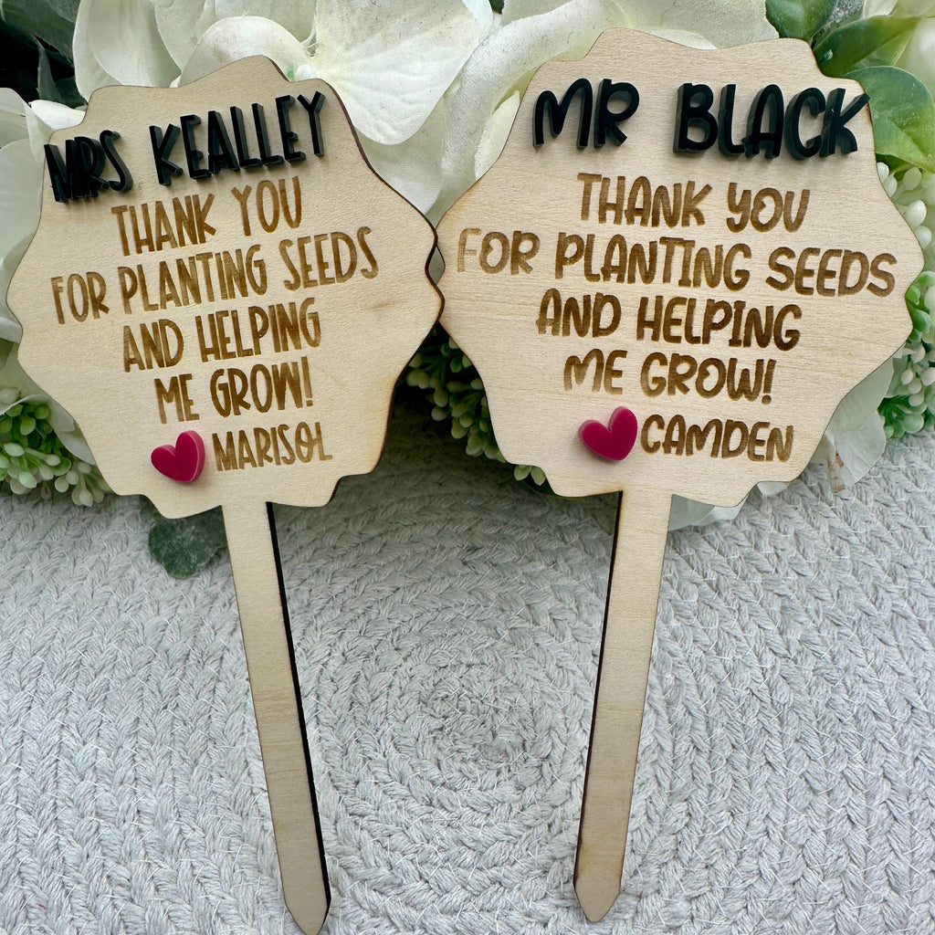 Teacher Plant Stake | Teacher Appreciation Gift | End of Year Gift |  Helping Me Grow | Boho Teacher Gift |  Wooden Plant Stake | Plant Sign
May include: Two wooden signs with the text &#39;Mrs Kealley Thank you for planting seeds and helping me grow! Marisol&#39; and &#39;Mr Black Thank you for planting seeds and helping me grow! Camden&#39; on them. Each sign has a small pink heart attached to it.
