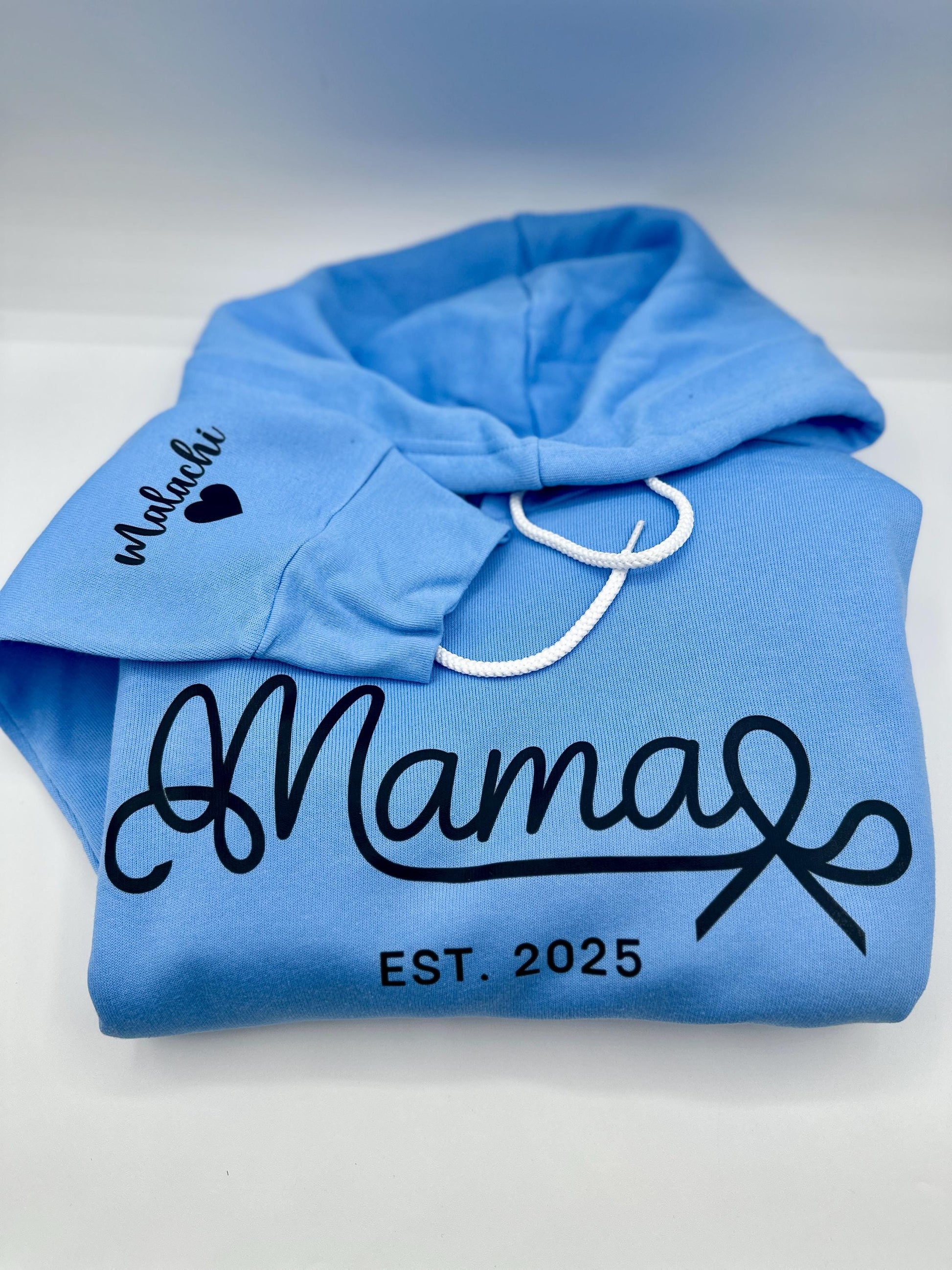 Mama Est Sweater| Custom Mama Est 2024 Sweater| Mom Sweatshirt| Mom Gift| New Mom Gift| DTF Fleece Hoodie Custom Sweater Bella + Canva

May include: A light blue hooded sweatshirt with the text &#39;Mama Est. 2025&#39; in black. The text &#39;Malachi&#39; with a black heart is on the left sleeve of the sweatshirt.